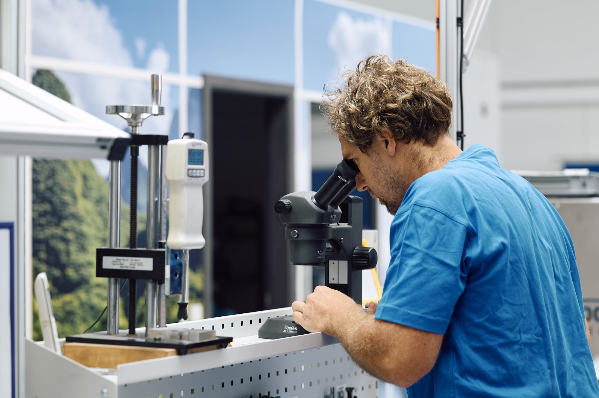 MICROQORE Auszubildender an der Werkbank mit Mikroskop und Werkzeugen